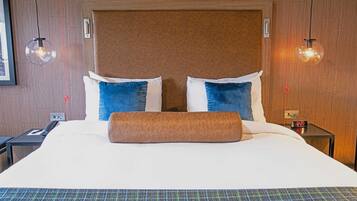 A hotel room with a large bed, two pillows, a blanket, a nightstand with a phone, and a wall clock.
