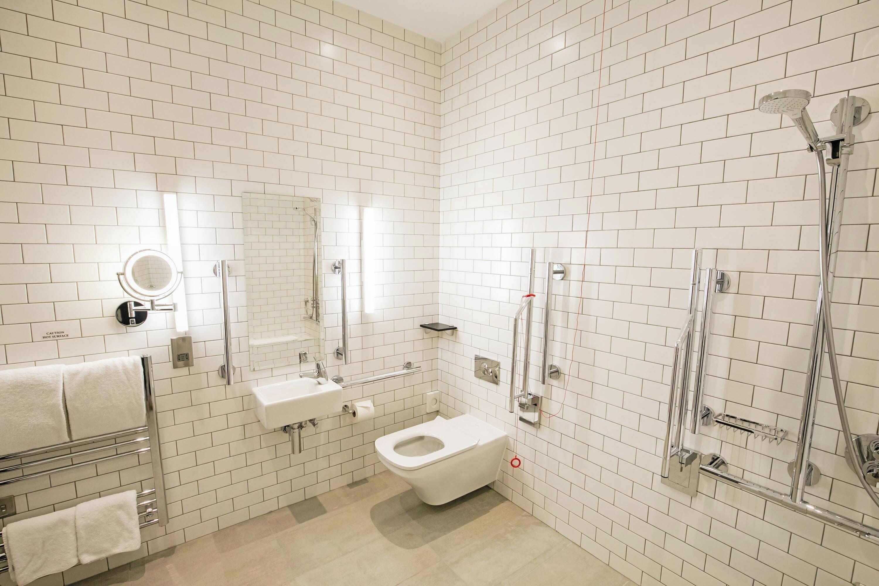 Een moderne badkamer met witte metrotegels, een wit toilet, een wastafel, een spiegel en een douche met glazen deur.