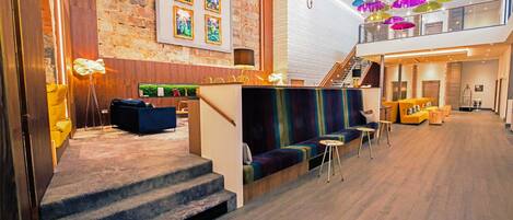 A modern hotel lobby with a stone wall, a staircase, a colorful seating area, and a chandelier.