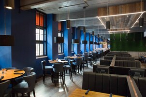 Um restaurante moderno com pé-direito alto, vigas aparentes e diversos tipos de assentos, incluindo cabines e mesas.