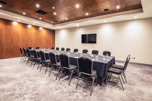 Un salón de conferencias con una larga mesa, sillas, un televisor de pantalla plana y techo de madera.