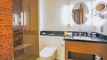 Un baño moderno con ducha de vidrio, inodoro, lavamanos con espejo y tocador de madera.