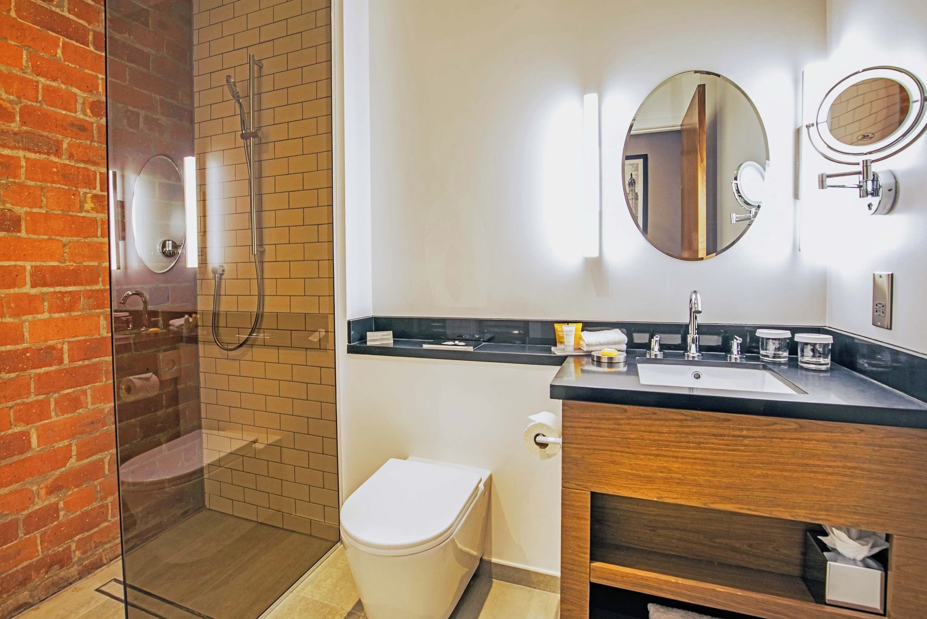A modern bathroom with a glass-enclosed shower, a white toilet, a wooden vanity with a sink, and a mirror.