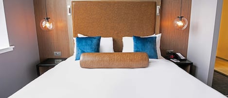 A hotel room with a large bed, two bedside tables, a wooden headboard, and two wall-mounted lamps.