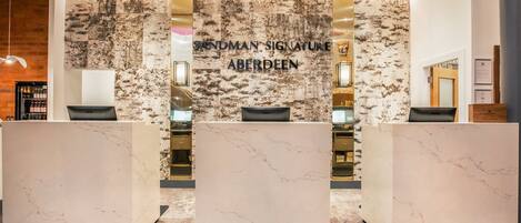 A reception area with a marble reception desk, a wall with the text "SANDMAN SIGNATURE ABERDEEN", and a wooden reception desk.