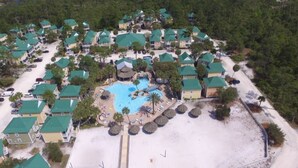 Vue aérienne d’un complexe hôtelier comprenant plusieurs bâtiments, une piscine centrale et une zone de plage.