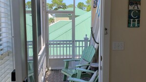 Une porte donnant sur un balcon où se trouve une chaise verte et une pancarte indiquant « Happy Hour ».