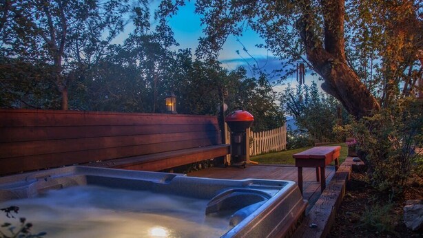 Ein Whirlpool mit Holzbänken und einer Holzterrasse, umgeben von Bäumen und einem Zaun.