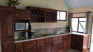 A kitchen with wooden cabinets, a microwave, a coffee maker, and a window with curtains. - Cuando el lujo y la comodidad estan rodeados de naturaleza (Los Angeles)
