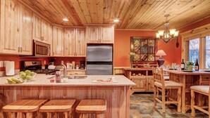 Una cocina con armarios de madera, una isla central con taburetes, un refrigerador y un comedor con sillas.