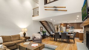 Ein großzügiger Wohnbereich mit Sofa, Couchtisch und Esstisch. Eine Küche mit modernen Geräten sowie eine Treppe zu einer oberen Ebene sind zu sehen.