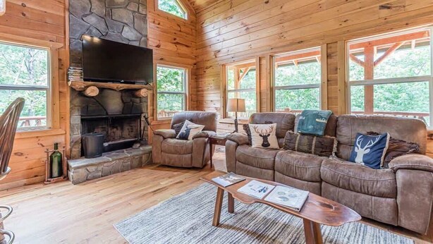 A cozy cabin interior with a stone fireplace, leather couches, and large windows. - CROSS CREEK HIDEAWAY | MOUNTAINS | PET FRIENDLY (Sautee Nacoochee)