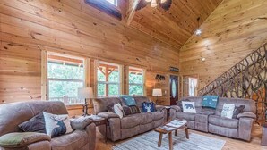 A wooden cabin interior with two sofas, a coffee table, and a staircase with a unique design. - CROSS CREEK HIDEAWAY | MOUNTAINS | PET FRIENDLY (Sautee Nacoochee)