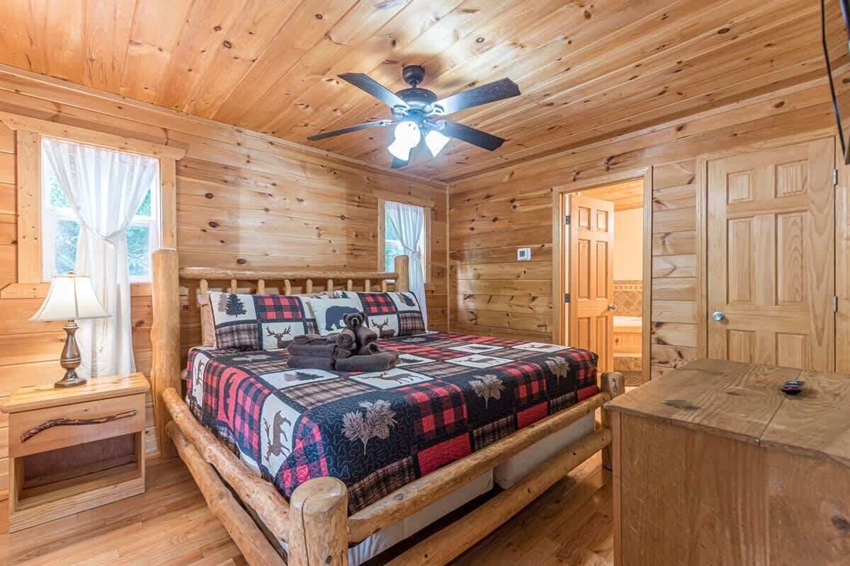 Une chambre dans une cabane en bois, avec un lit, un ventilateur de plafond, une table de chevet et une commode.