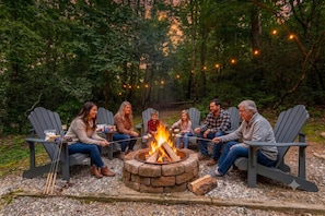 A group of people sitting around a campfire in an outdoor setting with Adirondack chairs and string lights. - Cross Creek Hideaway | Mountains & Pet Friendly (Sautee Nacoochee)