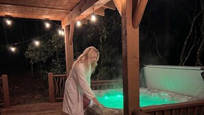 A person standing by a hot tub under a wooden deck at night. - CROSS CREEK HIDEAWAY | MOUNTAINS | PET FRIENDLY (Sautee Nacoochee)