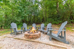 Un foyer entouré de quatre chaises Adirondack, installé sur une surface de gravier, avec une forêt en arrière-plan.
