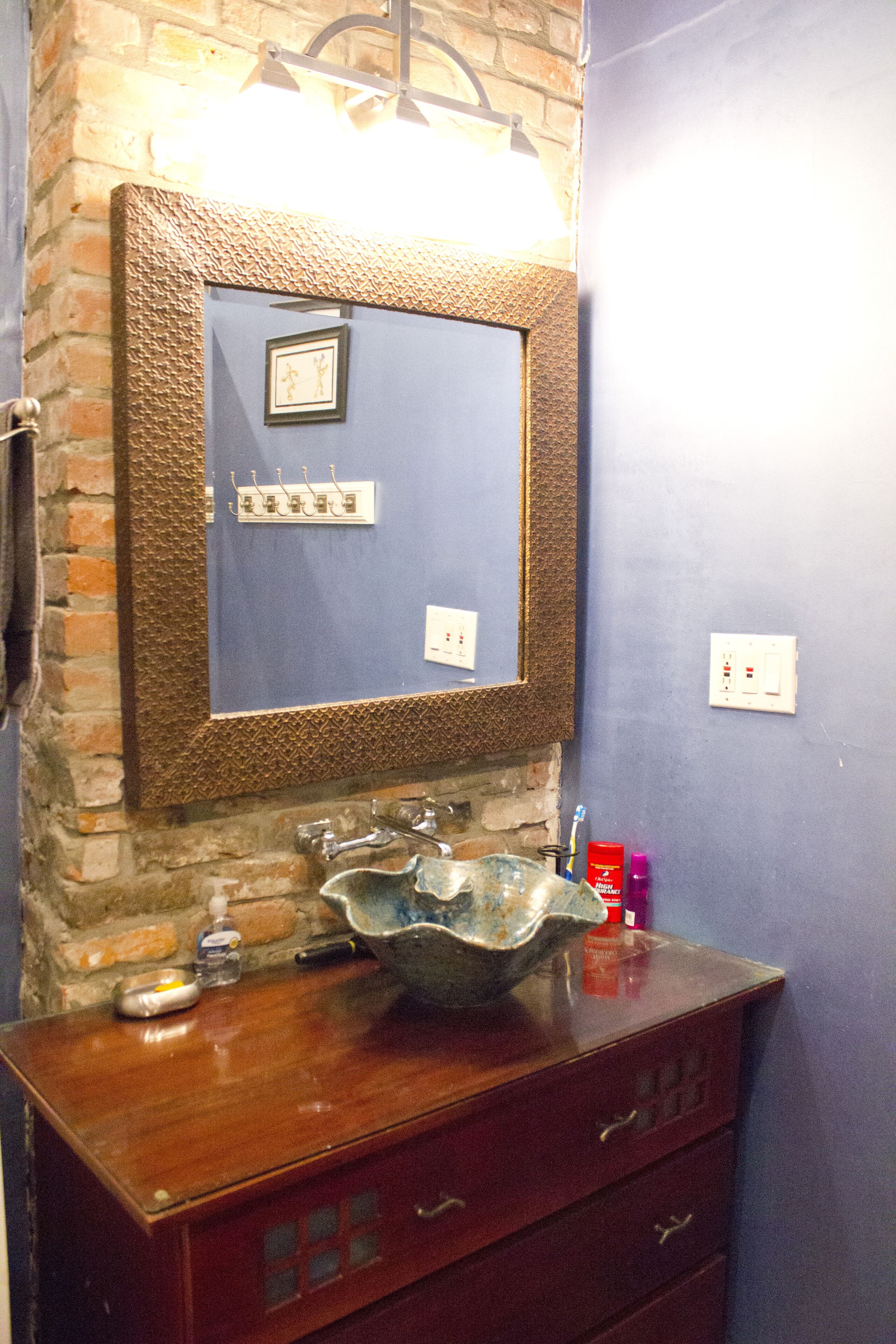 A bathroom with a stone wall, a wooden vanity, a sink, and a mirror.