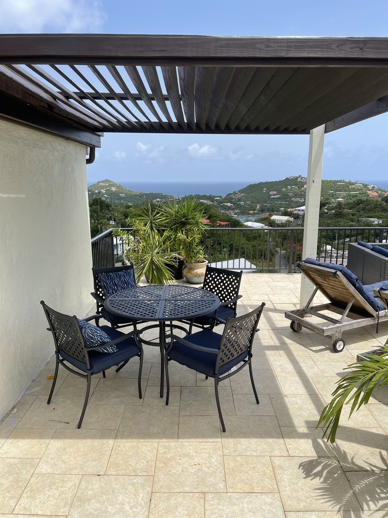 An outdoor patio with a table and chairs, a potted plant, and a view of the sea and hills.