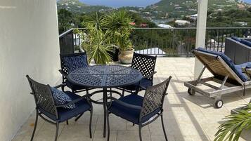 An outdoor patio with a table and chairs, a potted plant, and a view of the sea and hills.