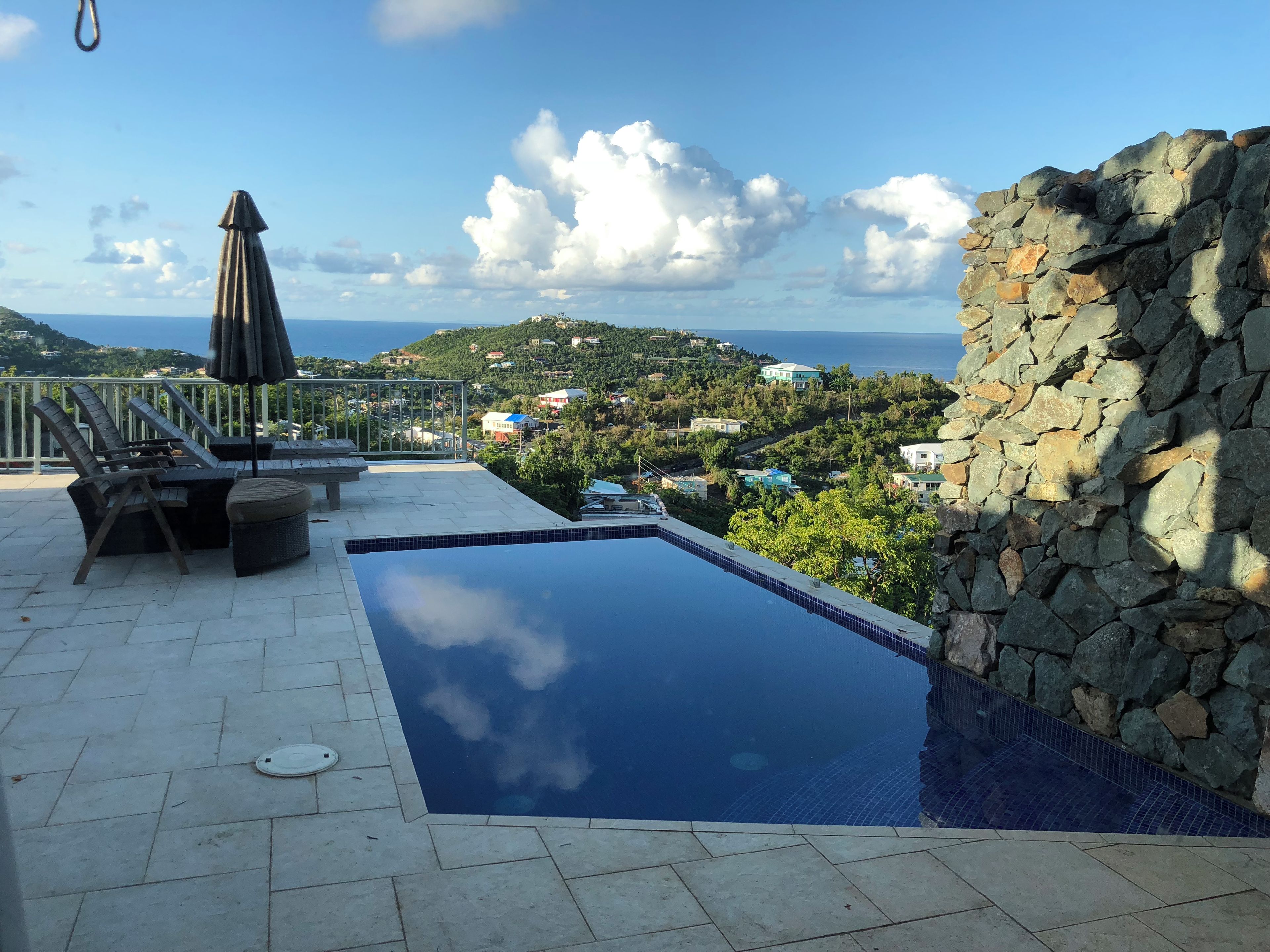 A swimming pool with a stone wall, lounge chairs, and an umbrella.