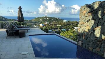 A swimming pool with a stone wall, lounge chairs, and an umbrella.