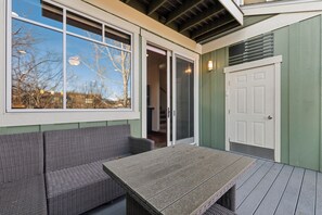 A covered patio with a table and two wicker sofas, a sliding glass door, and a white door.
