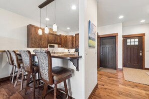 Cocina con gabinetes de madera, luces colgantes y una barra con taburetes.