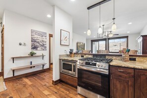 A modern kitchen with built-in appliances, wooden flooring, and pendant lighting.