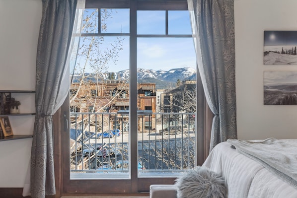 A bedroom with a large window, a bed, a fur throw, and a framed picture on the wall.