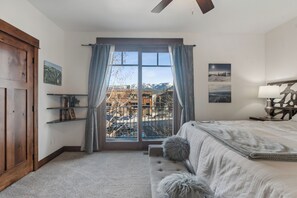 Una camera da letto con un'ampia finestra, un letto, una ventola a soffitto e un armadio in legno.