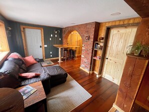A cozy living room with a dark leather sofa, a wooden coffee table, and a brick wall. - Newly Renovated - Cozy and Quiet Apt Style Cabin on Yellowstone River (Gardiner)