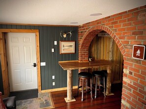 A room with a wooden bar, two stools, a fireplace, and a door. - Newly Renovated - Cozy and Quiet Apt Style Cabin on Yellowstone River (Gardiner)