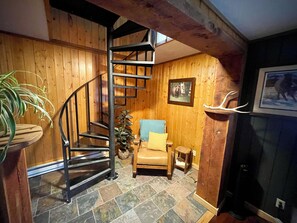 A wooden interior with a spiral staircase, a blue armchair, a small table, and a fireplace.