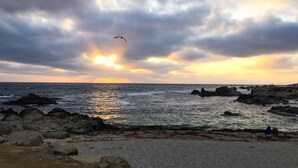 Una costa rocosa con el océano y un atardecer al fondo.
