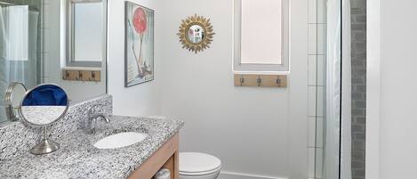 Un baño con encimera de granito, inodoro, ducha con puertas de vidrio, espejo y espejo con forma de sol en la pared.