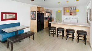 A compact kitchen with a central island, bar stools, a bench, and a ceiling fan. - Perfect Purple Palace Folly Vacation Apt C (Folly Beach)