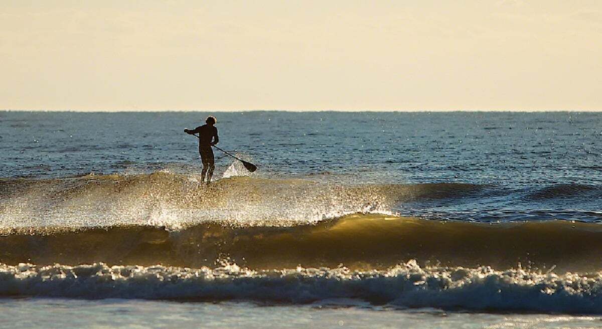 Una persona haciendo paddleboard en un mar tranquilo durante la puesta de sol.