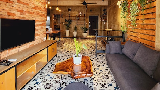 A modern living room with a brick wall, a flat-screen TV, a gray sofa, a coffee table with a plant, and patterned floor tiles. - Scenic Valley Suite (Ho Chi Minh City)