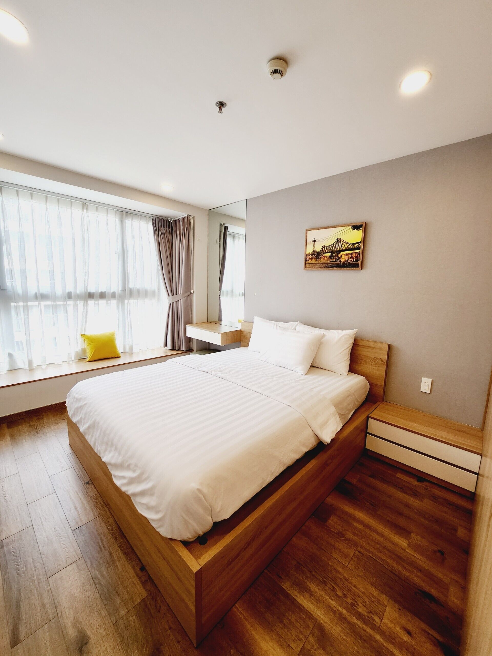 A modern bedroom with a wooden bed, a bedside table, a mirror, and a window with curtains.