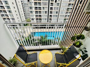 Un balcón con dos sillas de malla negra y una mesa amarilla, con vistas a una piscina y edificios altos.