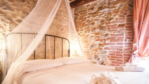 A bed with a white canopy and pillows, a brick wall, and a window with curtains. - B&B Antica Gabella (Castiglione del Lago)