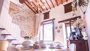 A dining area with a round table set for four, a chandelier, and a view of the outside through a window. - B&B Antica Gabella (Castiglione del Lago)