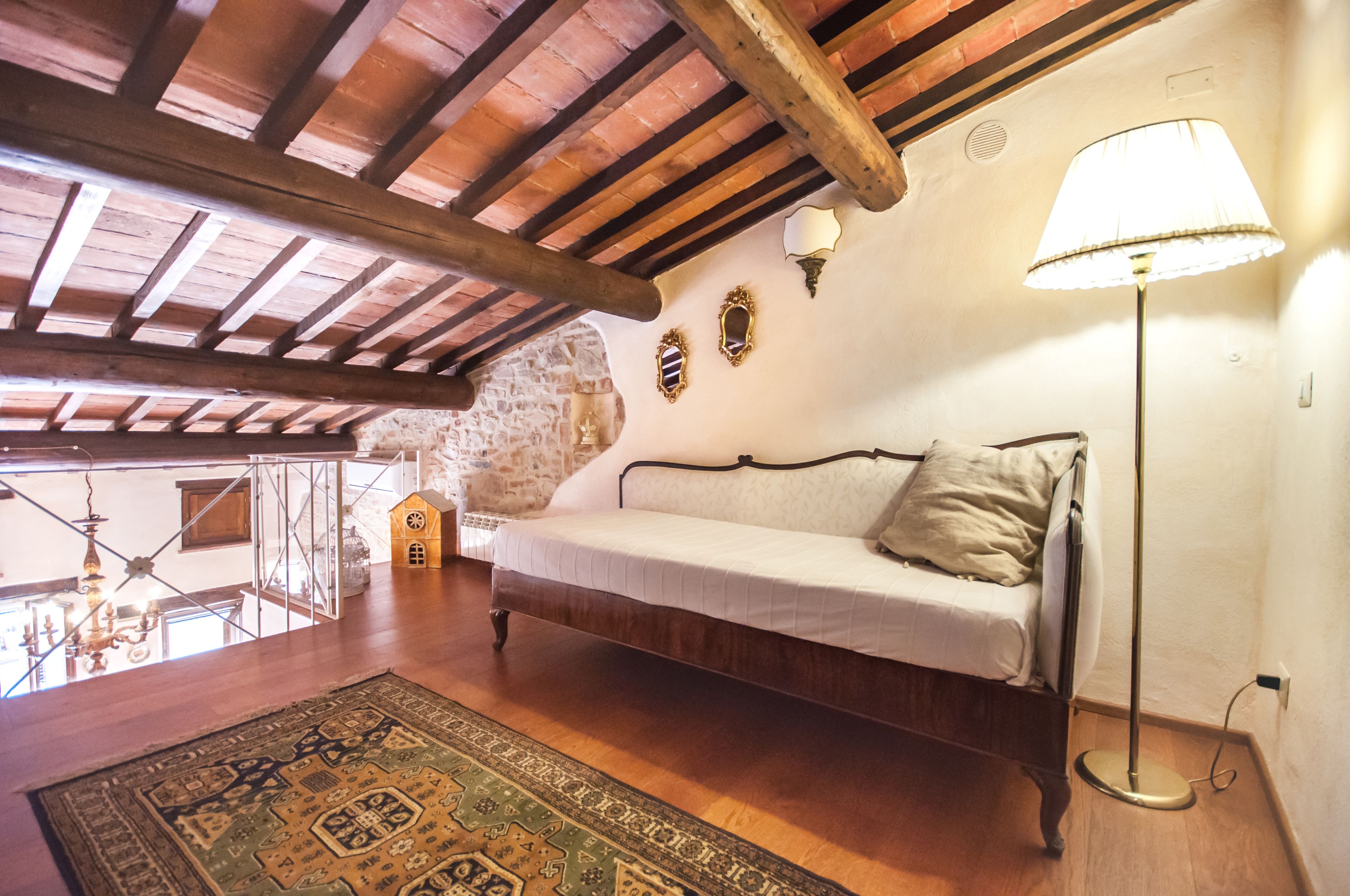 A cozy room with a wooden ceiling, a white sofa, a patterned rug, and a lamp.