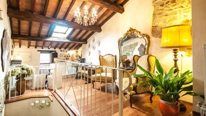 A spacious living area with a wooden ceiling, a chandelier, and a stone wall. There is a staircase leading to an upper level, and a large mirror on the wall. - B&B Antica Gabella (Castiglione del Lago)