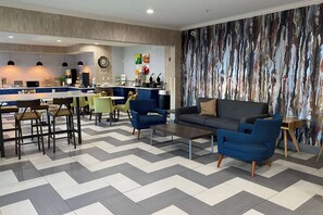 A modern living area with a sofa, chairs, a coffee table, a kitchen in the background, and a patterned wall.