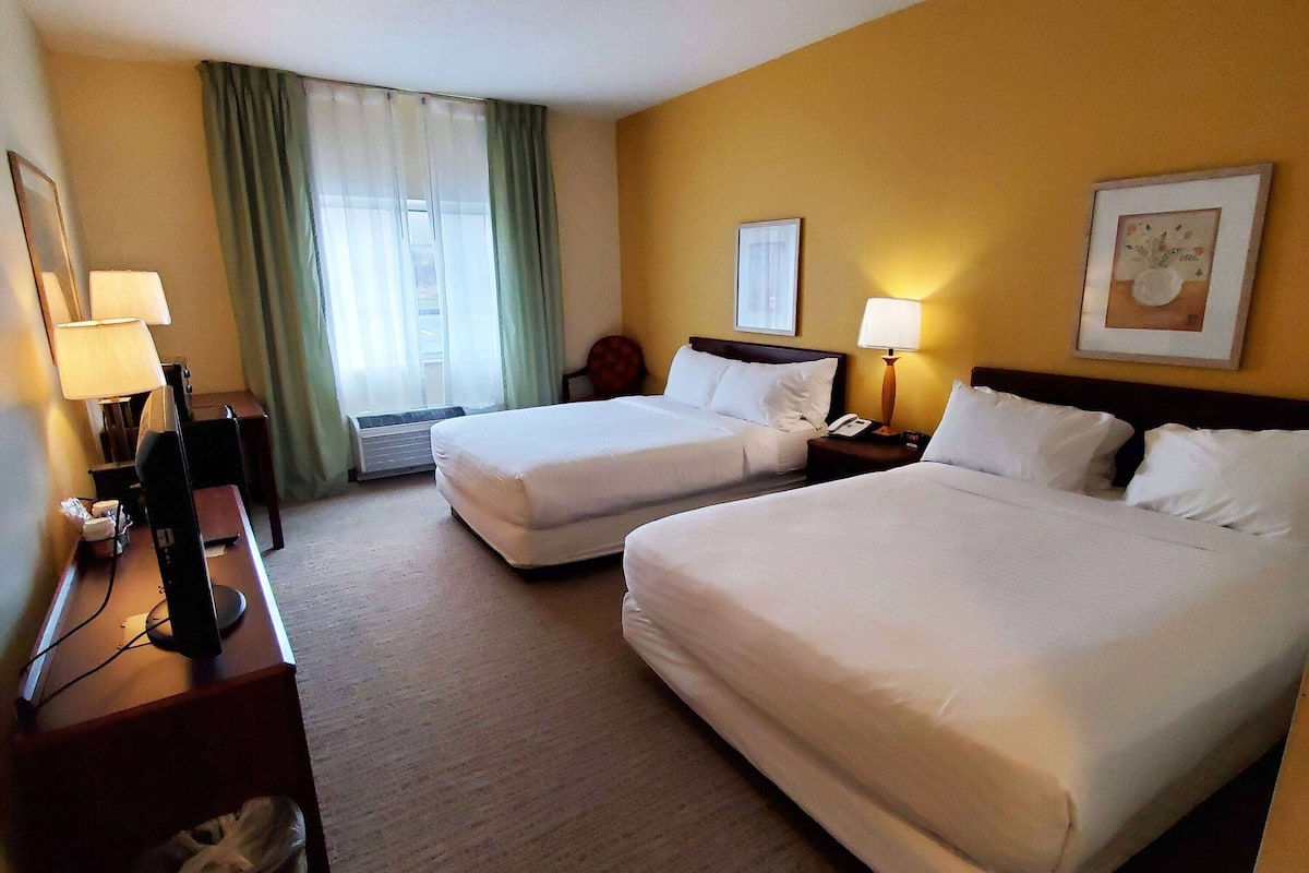 A hotel room with two beds, a desk with a computer, a chair, and a window with curtains.