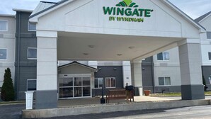 A Wingate by Wyndham hotel entrance with a covered walkway, a bench, and a trash can. - Wingate by Wyndham Uniontown (Uniontown)