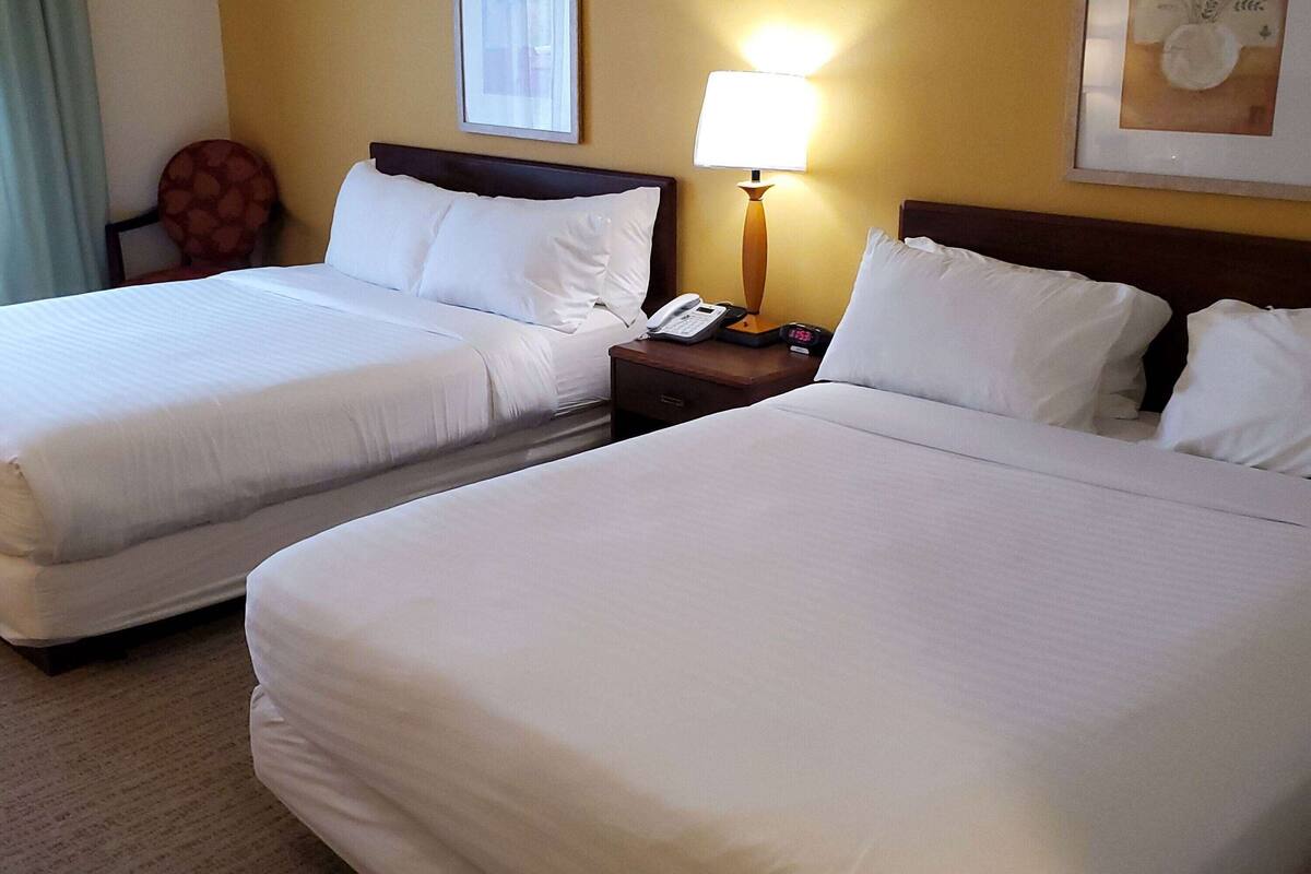 A hotel room with two beds, a nightstand with a lamp, a telephone, and a chair.