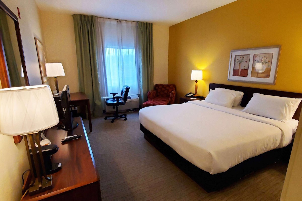 A hotel room with a bed, desk, chair, and a window with curtains.